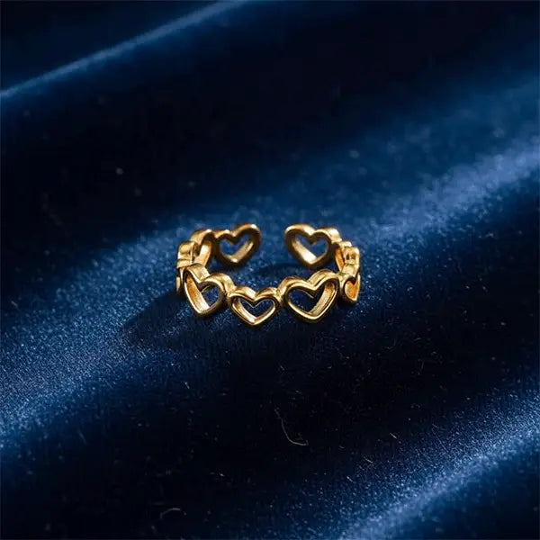 Gold heart-pattern band ring placed on deep blue velvet fabric with elegant lighting.