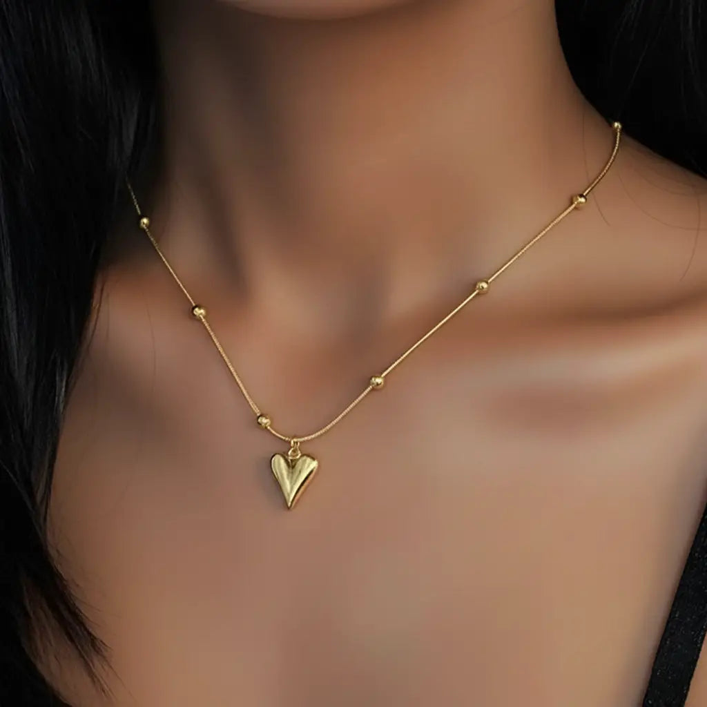 Gold heart pendant necklace with beaded chain worn on a woman's neck, showcasing the elegant minimalist design.