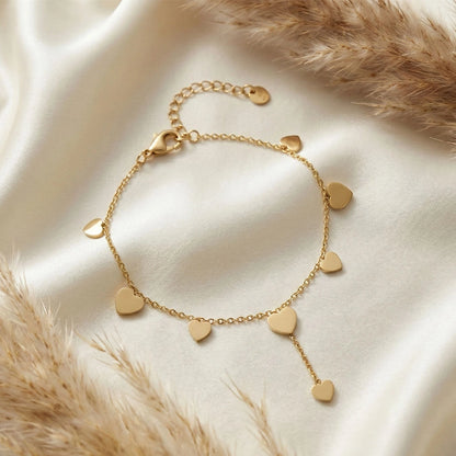 Gold anti-tarnish heart trail bracelet with multiple heart charms arranged on soft ivory fabric with dried florals.