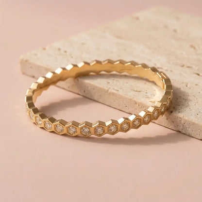 Hexagon crystal gold bracelet with diamond-like stones placed on beige stone surface, sleek geometric design.