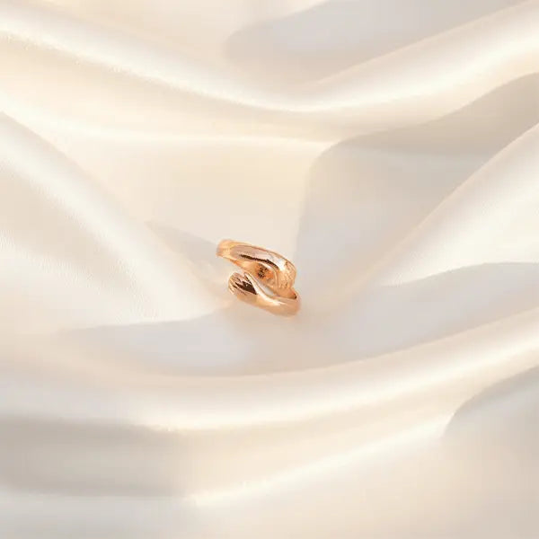 Rose gold hug ring with an open wrap design displayed on soft satin fabric in warm light.