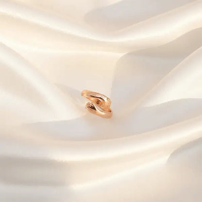 Rose gold hug ring with an open wrap design displayed on soft satin fabric in warm light.