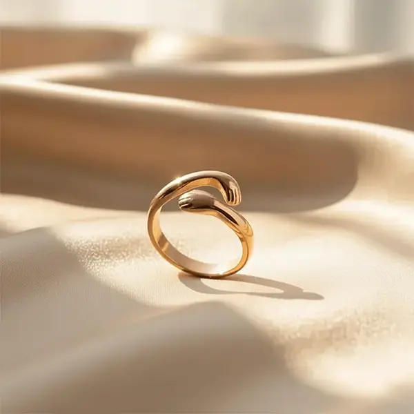 Rose Gold open hug ring with curved wrap-around design placed on silky beige fabric under natural sunlight.