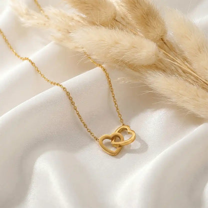 Interlock heart gold pendant necklace placed on white satin fabric with soft pampas grass, highlighting the minimal heart design and anti-tarnish finish.