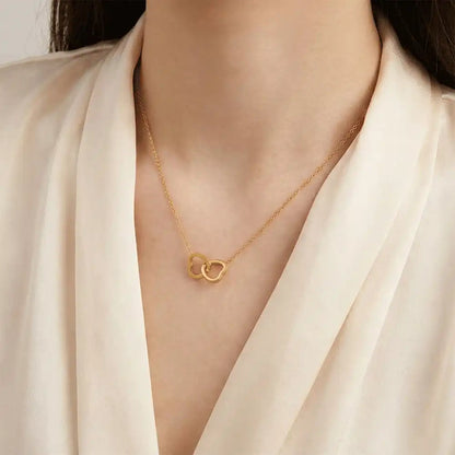 Model wearing an interlocking heart gold pendant necklace on a delicate chain, styled with a neutral outfit for an elegant everyday look.