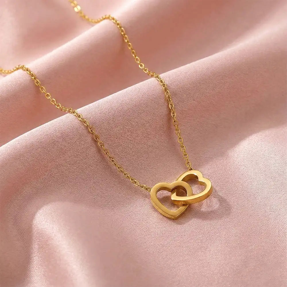 Close-up of interlock heart gold pendant necklace displayed on blush pink satin fabric, showcasing the smooth heart shape and polished gold shine.