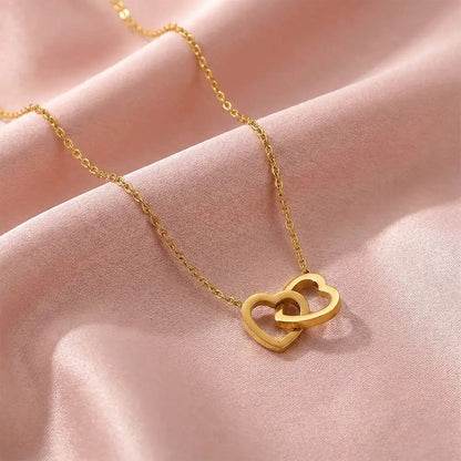 Close-up of interlock heart gold pendant necklace displayed on blush pink satin fabric, showcasing the smooth heart shape and polished gold shine.