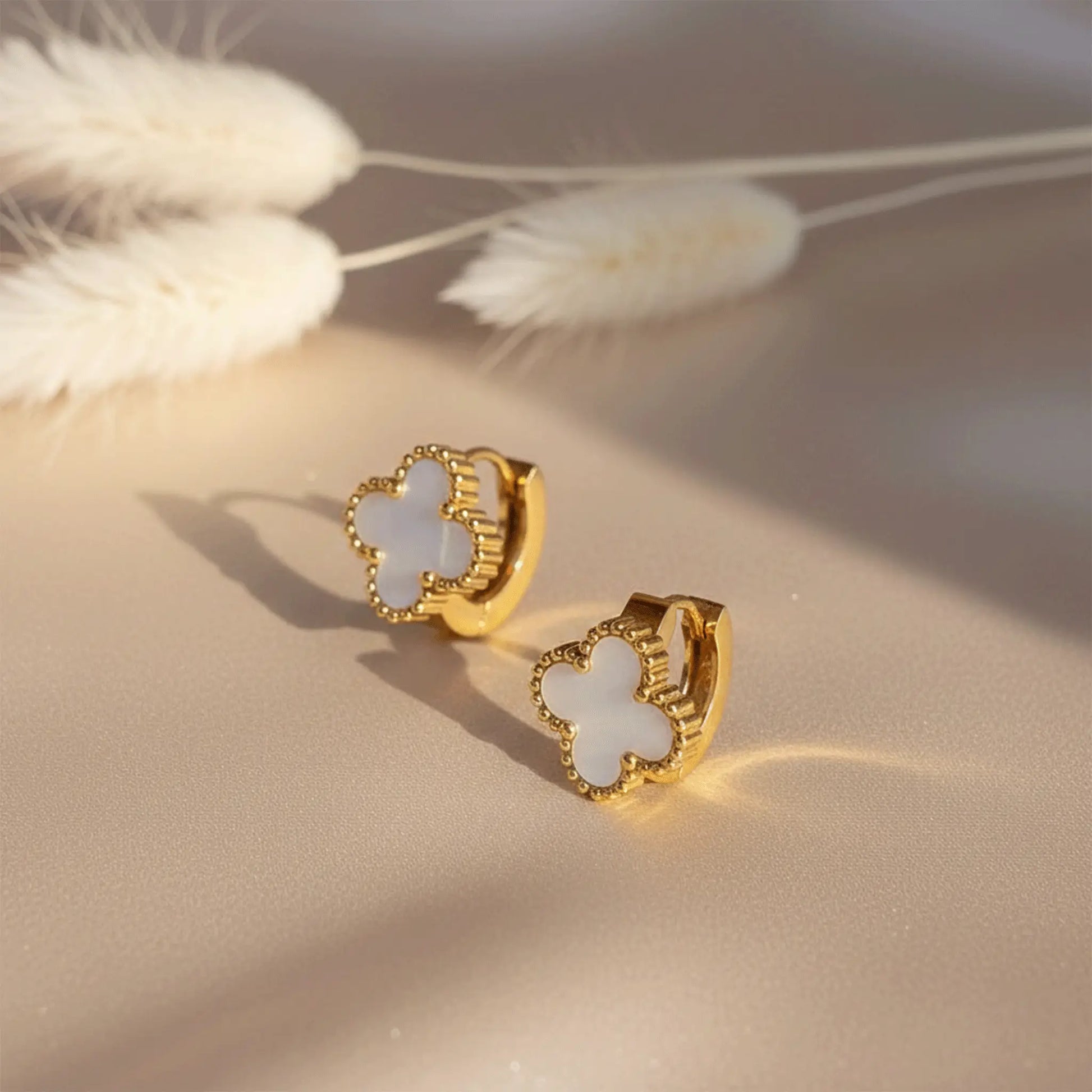 Ivory Clover Hoops earrings with mother-of-pearl clover design placed on beige satin fabric with soft sunlight and pampas grass