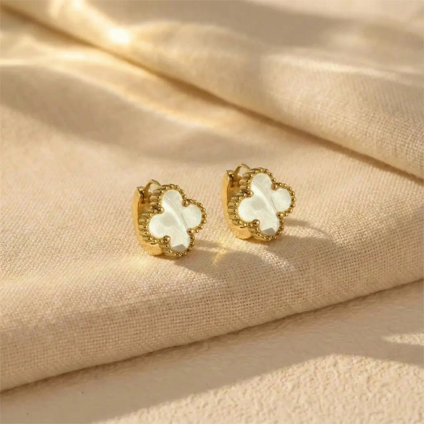 Pair of Ivory Clover Hoops earrings displayed on neutral fabric background with soft luxury lighting