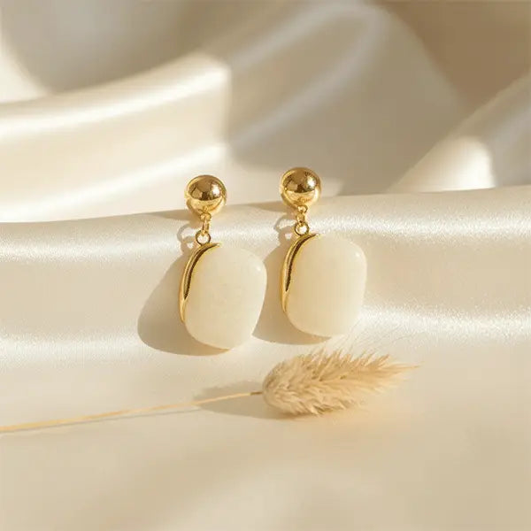 ivory stone dangle earrings displayed on beige satin fabric with soft sunlight and dried phalaris grass
