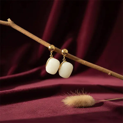 Ivory stone earrings hanging on a branch with maroon velvet background and dried phalaris grass prop