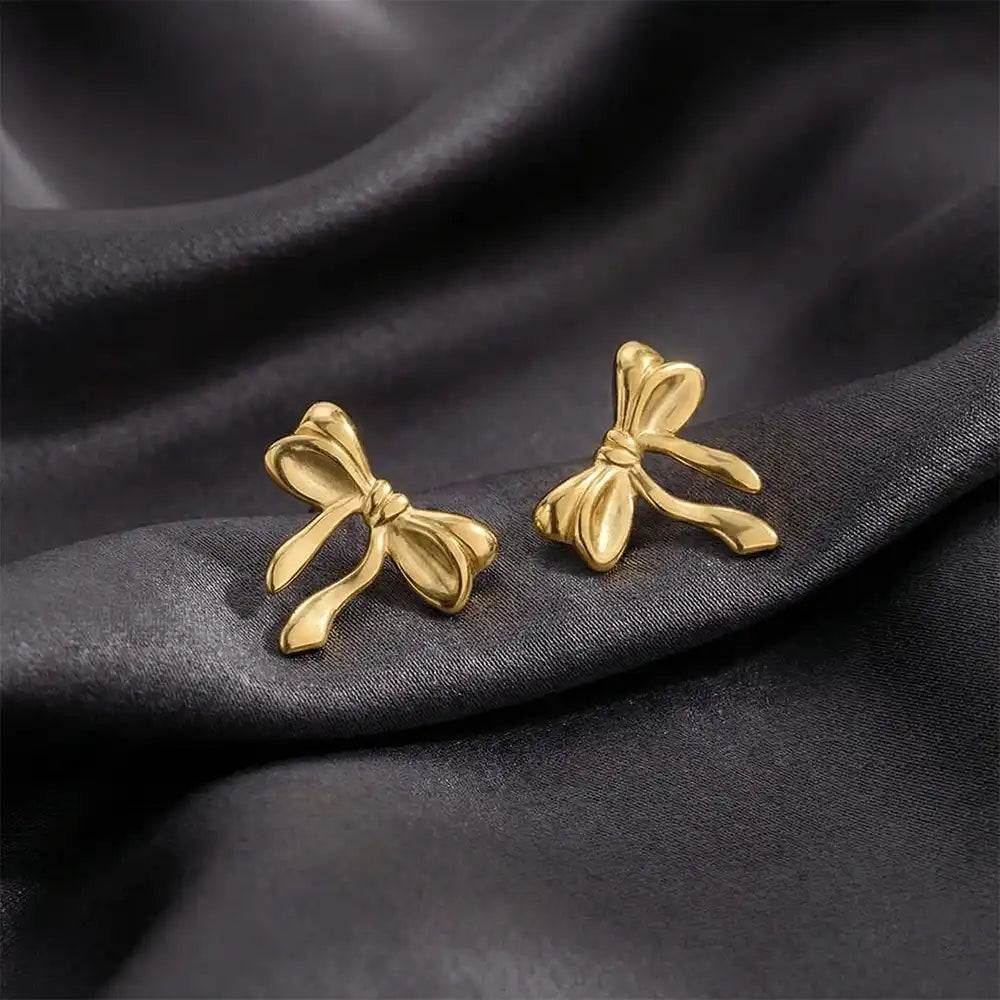 Gold knot bow stud earrings displayed on black satin fabric, highlighting the smooth bow design and polished anti-tarnish finish.