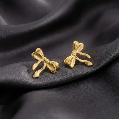 Gold knot bow stud earrings displayed on black satin fabric, highlighting the smooth bow design and polished anti-tarnish finish.