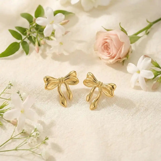 Anti-tarnish gold knot bow stud earrings placed on light fabric with white flowers, showcasing a delicate knot bow shape and soft shine.