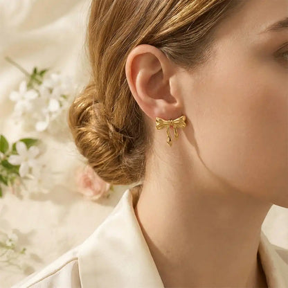 Model wearing gold knot bow stud earrings, styled with a low bun hairstyle and floral background for an elegant, feminine look.
