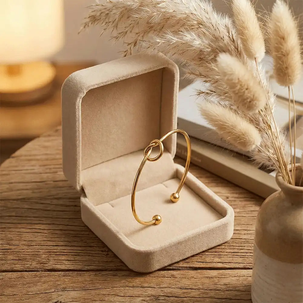 Anti-tarnish gold knot bangle displayed inside a beige jewelry box with pampas grass accents, styled for a premium gifting look.
