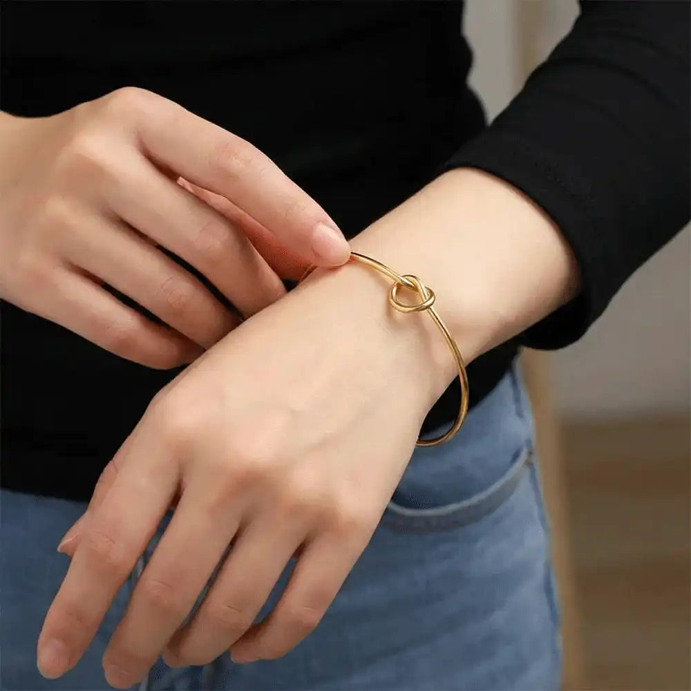 Model wearing a gold knot bangle bracelet on the wrist, showing the adjustable open cuff design for everyday styling.
