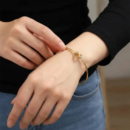 Model wearing a gold knot bangle bracelet on the wrist, showing the adjustable open cuff design for everyday styling.