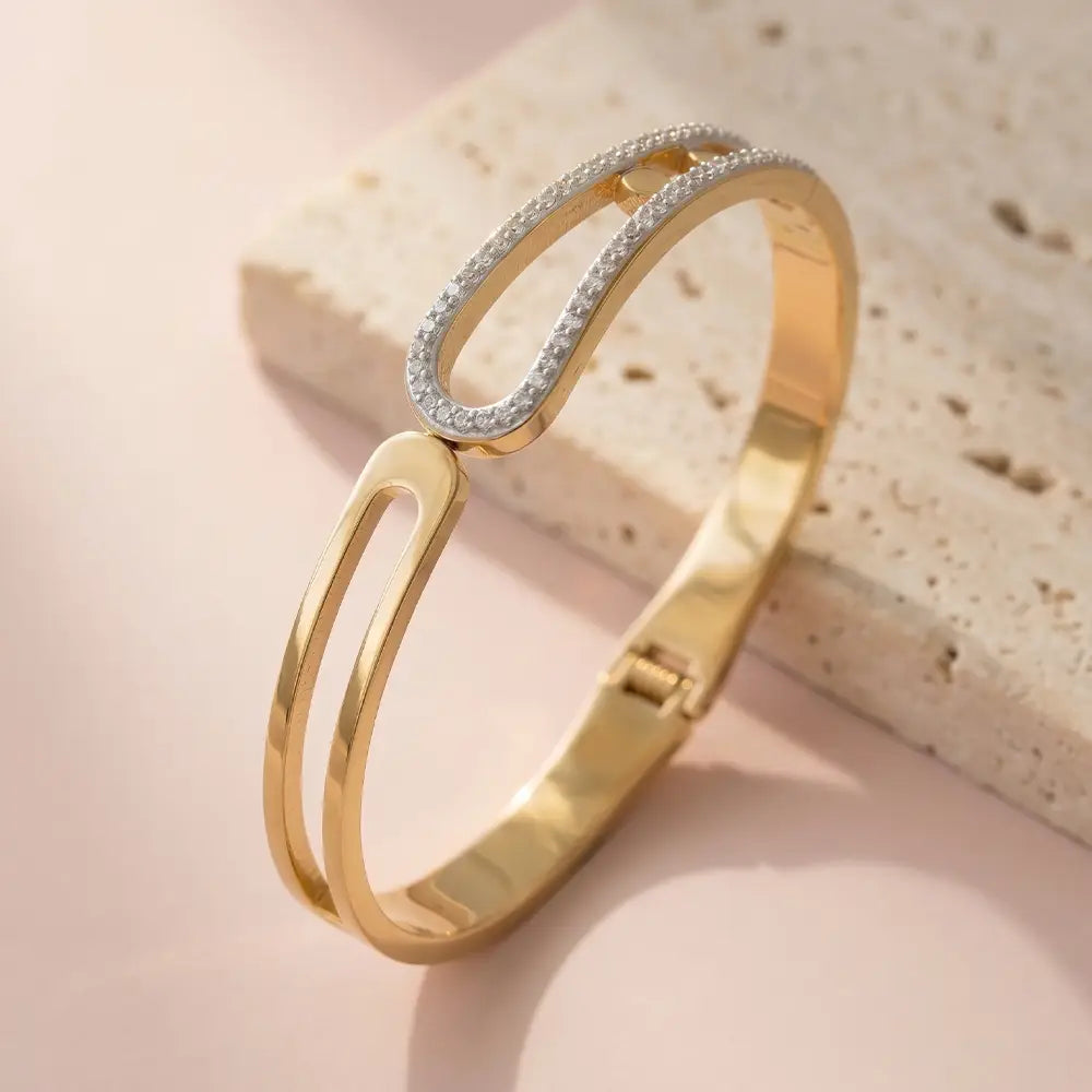 Loop crystal gold bracelet with pavé crystal loop detail placed on neutral stone surface.
