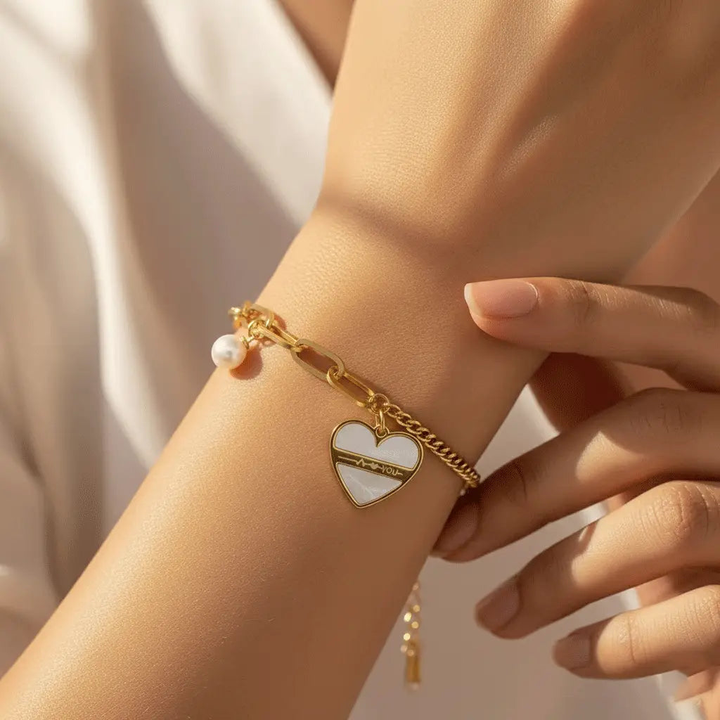 Gold Love Chain Bracelet featuring a white heart charm and pearl drop worn on wrist in warm natural light.