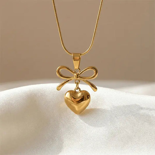 Love Knot Pendant anti-tarnish necklace with bow and heart charm displayed on soft satin fabric with warm neutral background