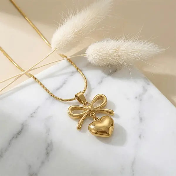 Love Knot Pendant anti-tarnish bow and heart charm necklace placed on marble surface with dried pampas grass