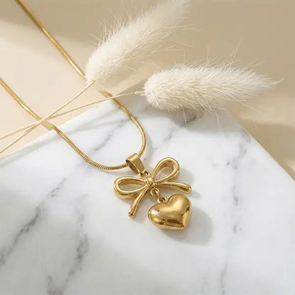 Love Knot Pendant anti-tarnish bow and heart charm necklace placed on marble surface with dried pampas grass