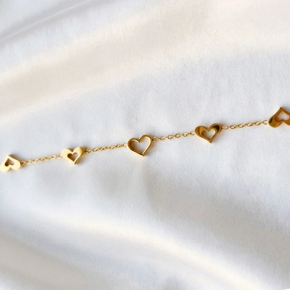 Love Loop Bracelet – Anti-Tarnish, gold bracelet with open heart charms styled on soft white satin fabric.