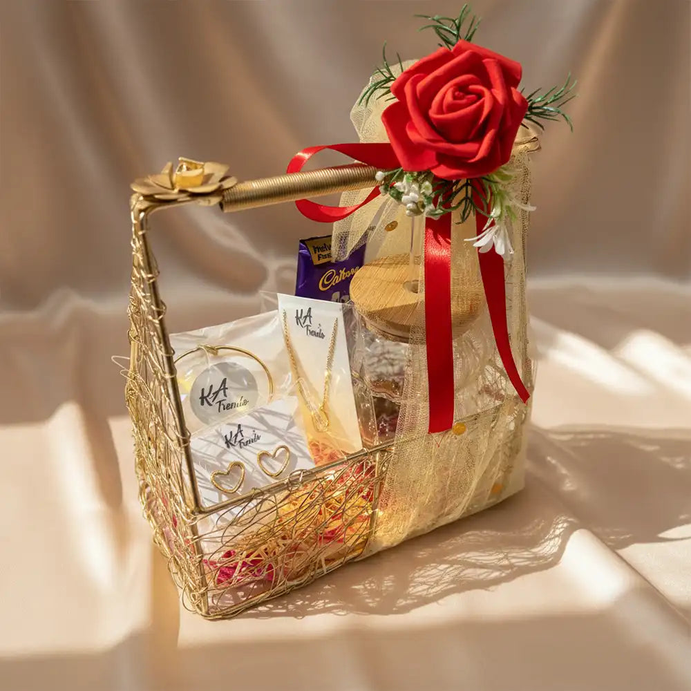 Luxe Valentine Special hamper with anti-tarnish heart earrings, bracelet, necklace, chocolates, and a decorative glass jar, arranged in a golden basket with red rose and ribbon on a satin background.