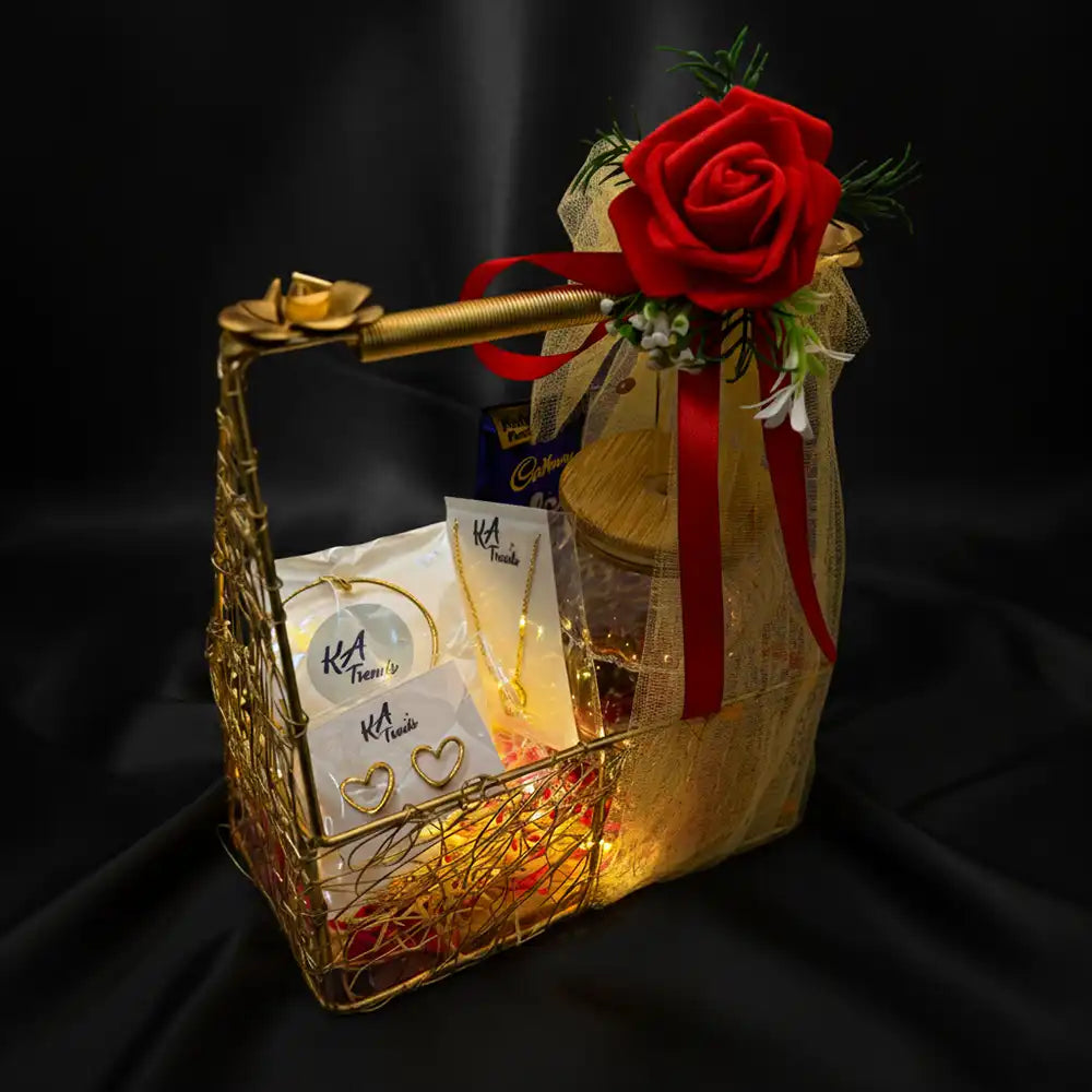 Premium Valentine Special anti-tarnish jewellery hamper with heart earrings, bracelet, necklace, chocolates, and glowing lights, presented in a gold basket with red rose on a black backdrop.