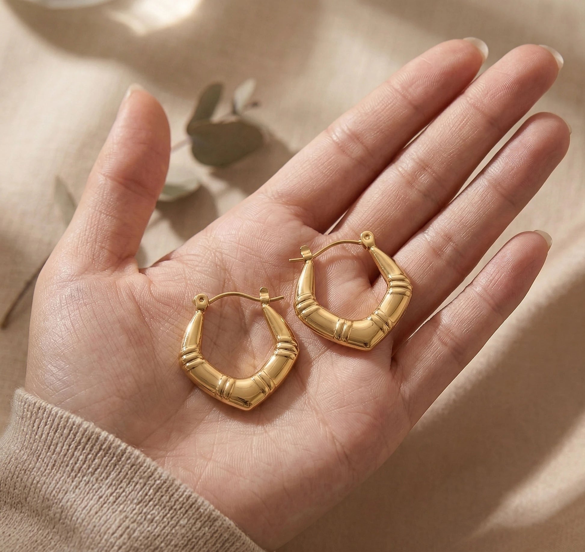 Luxe Arc Hoops held in a hand with a neutral background