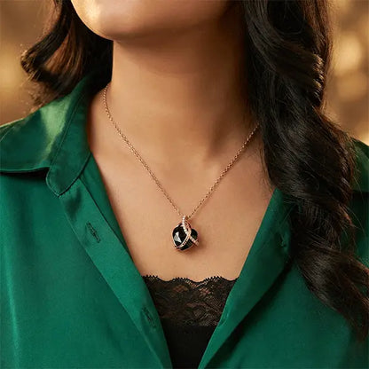 Woman wearing a black heart pendant necklace with rose gold detailing, styled with a green outfit.