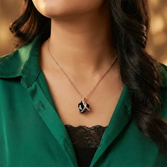 Woman wearing a black heart pendant necklace with rose gold detailing, styled with a green outfit.