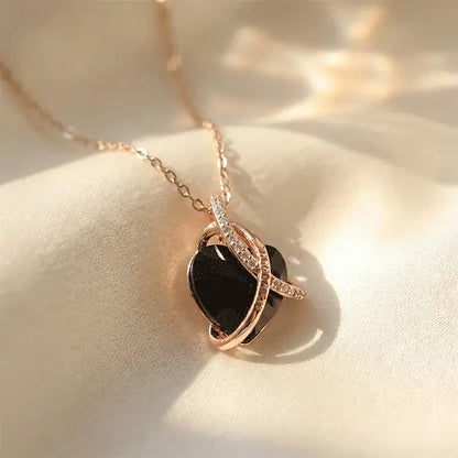Black heart pendant necklace with rose gold crystal accents displayed on soft cream satin under natural sunlight.