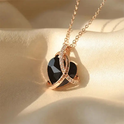 Close-up of a faceted black heart pendant wrapped in rose gold crystal-studded bands on a satin background.