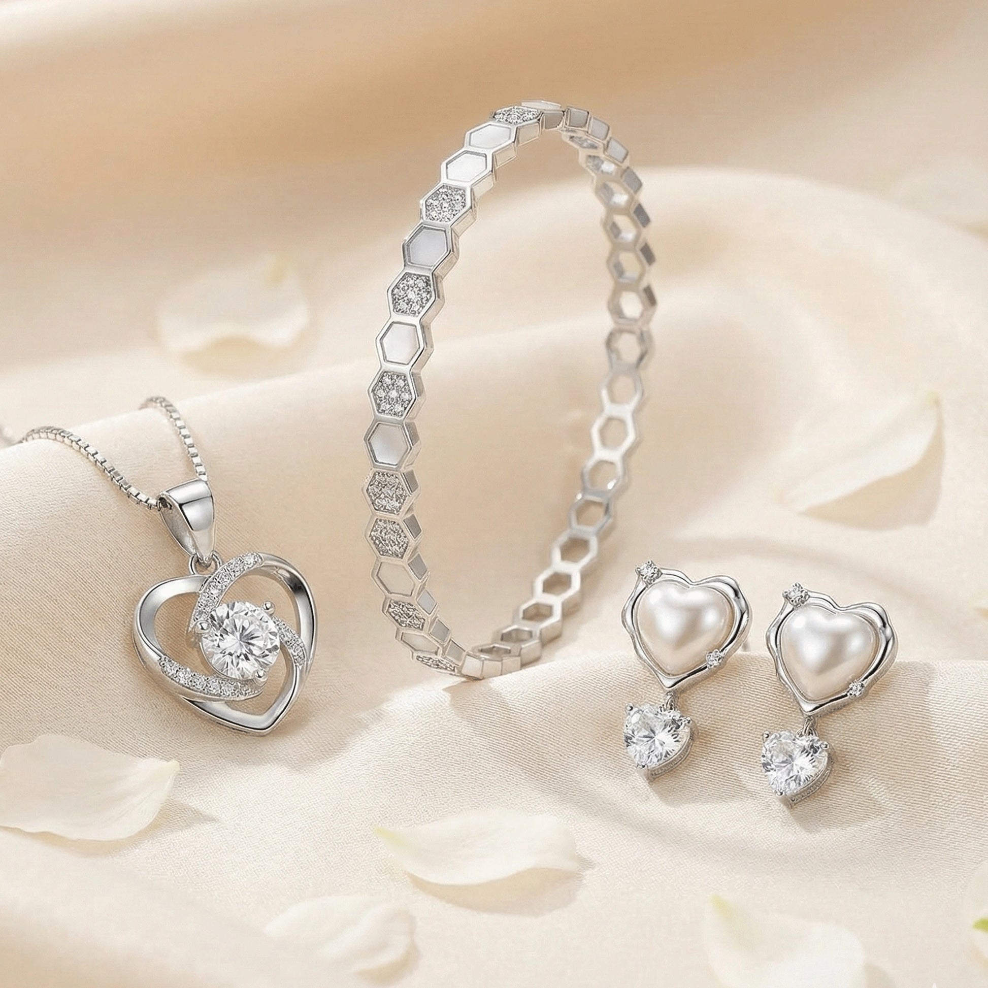 Elegant silver jewelry set with a crystal heart pendant, hexagon-link bracelet, and heart-shaped pearl drop earrings styled on a soft neutral satin background.