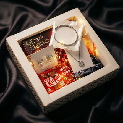 Luxury Valentine hamper with anti-tarnish silver heart jewelry, chocolates, warm fairy lights, and premium gift packaging on dark satin background