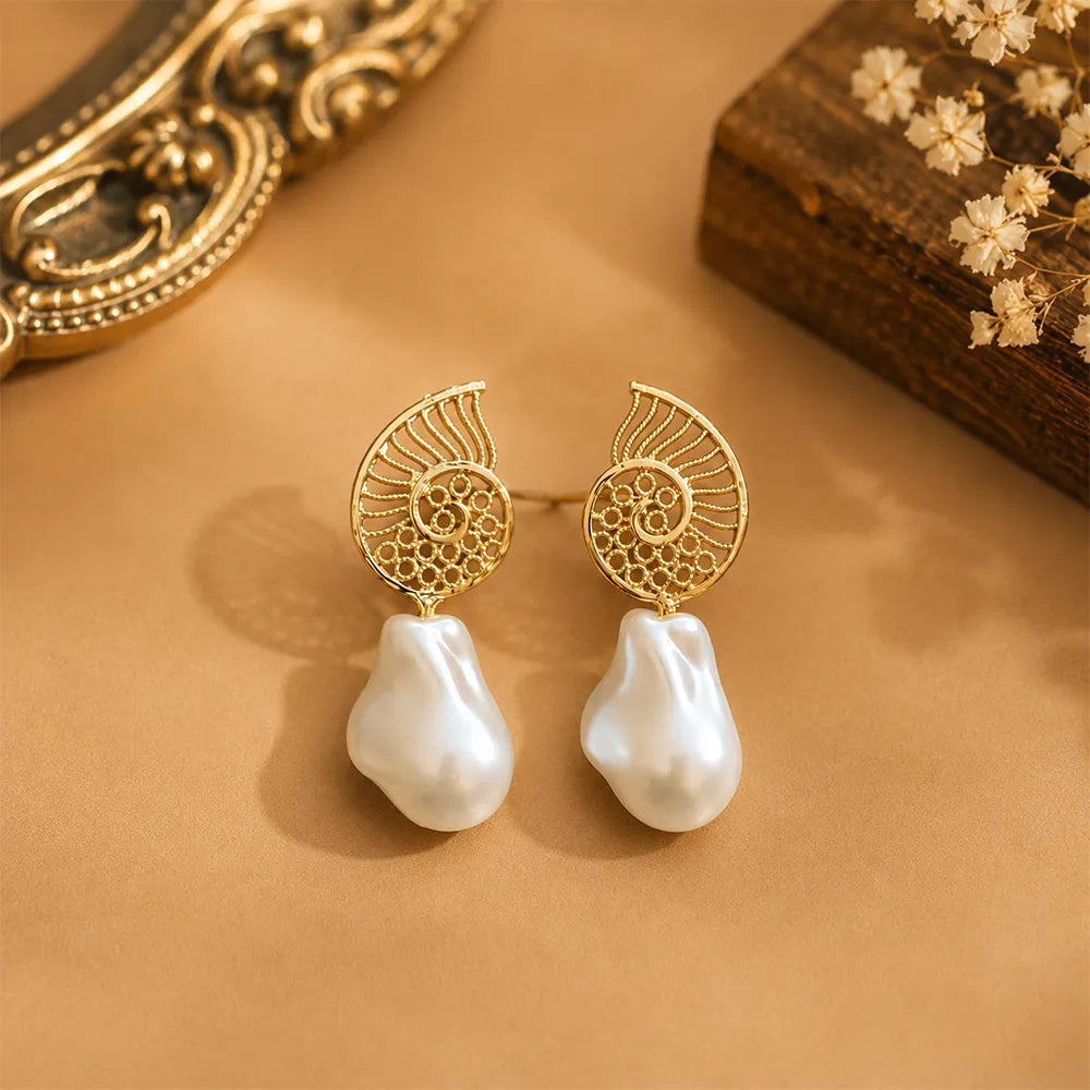 Pair of Ocean Spiral anti tarnish brass earrings featuring gold-toned spiral motifs and irregular baroque pearl drops on a warm beige background.
