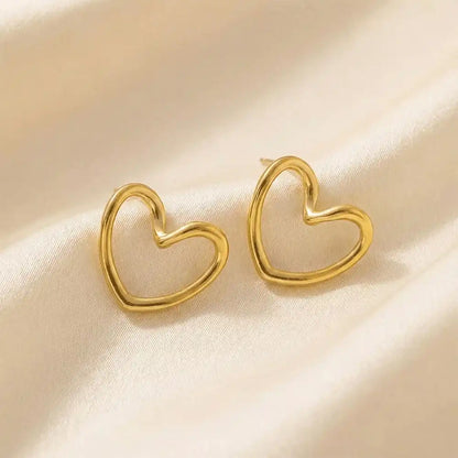 Anti-tarnish open heart gold stud earrings displayed on beige satin fabric, showcasing the minimal heart shape and glossy gold tone.