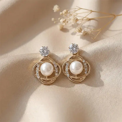 Orbit Pearl Earrings anti-tarnish stud earrings with pearl and crystal detailing placed on beige satin fabric with soft floral accents