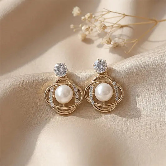 Orbit Pearl Earrings anti-tarnish stud earrings with pearl and crystal detailing placed on beige satin fabric with soft floral accents