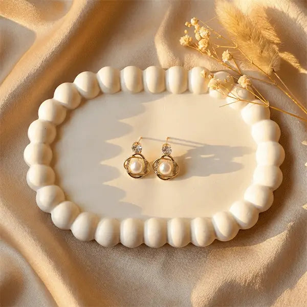 Orbit Pearl Earrings anti-tarnish pearl stud earrings displayed on white ceramic plate over beige satin cloth with minimal dried flowers