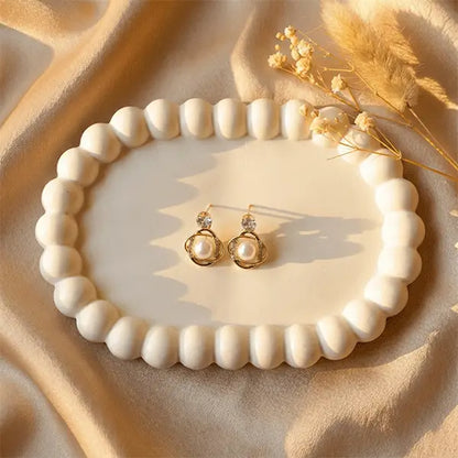Orbit Pearl Earrings anti-tarnish pearl stud earrings displayed on white ceramic plate over beige satin cloth with minimal dried flowers