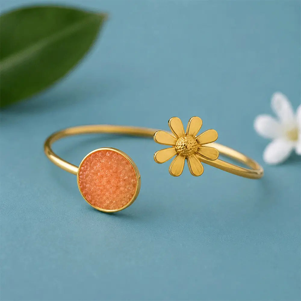 Peach Blossom anti tarnish brass bracelet with a peach druzy stone and gold-toned daisy flower motif on a pastel blue background.