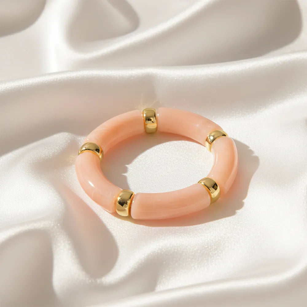 Peach resin bracelet with gold accents displayed on a satin cloth.