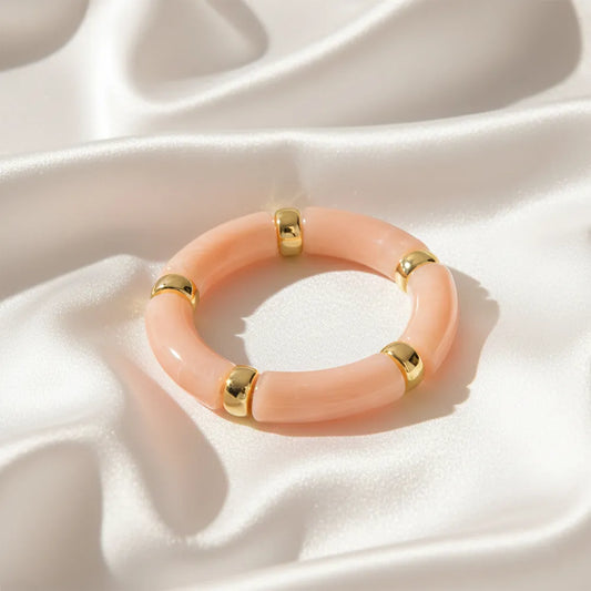 Peach resin bracelet with gold accents displayed on a satin cloth.