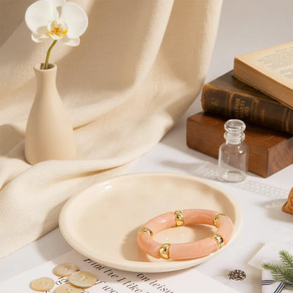 Peach resin bracelet with gold accents displayed on a beige plate with books, a vase, and small decor items.
