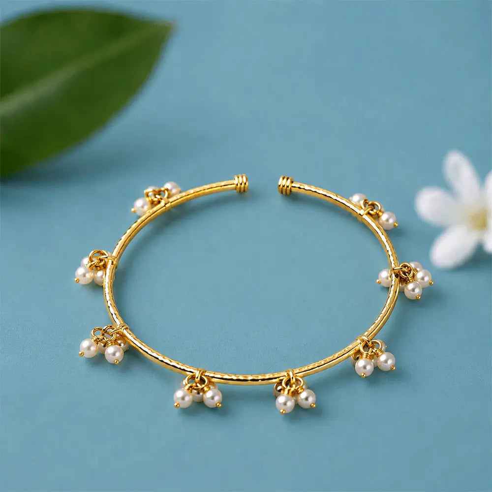 Pearl Charm anti tarnish brass bracelet with multiple dangling pearl charms and a textured gold-toned open cuff design on a pastel blue background.