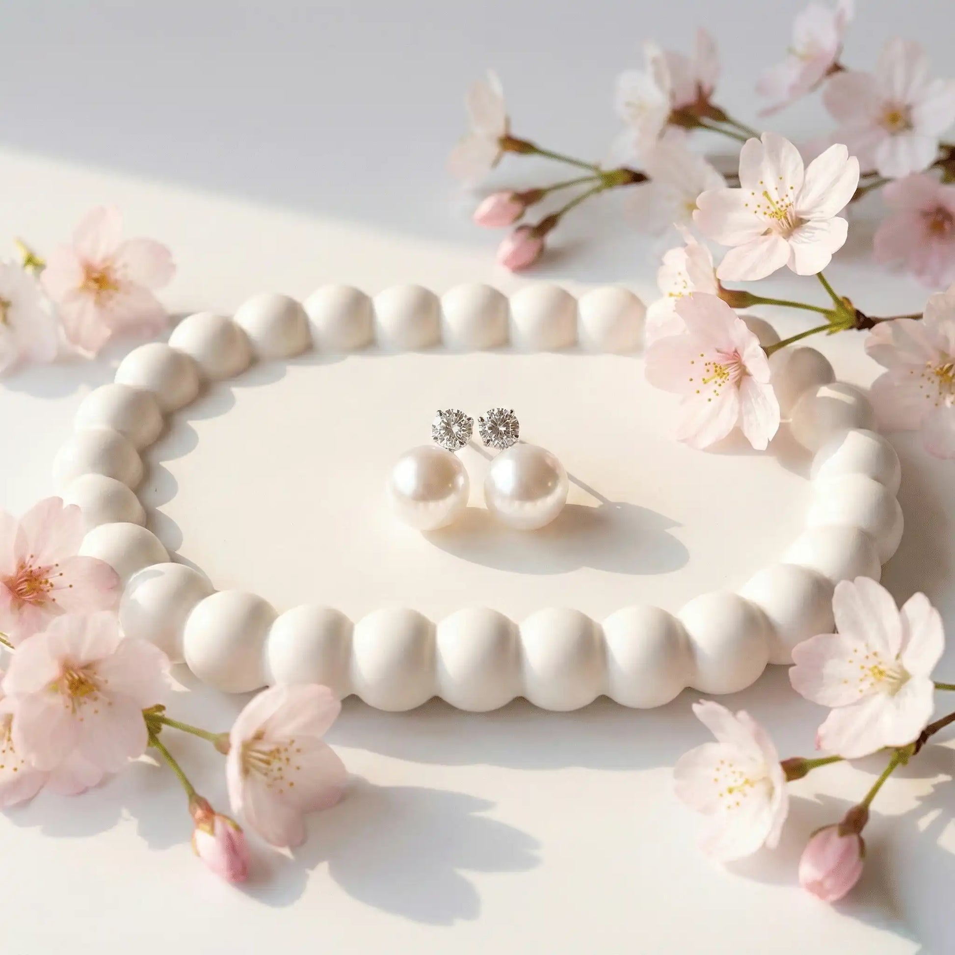 Pearl Drop Earrings with crystal studs displayed on white ceramic tray with soft sunlight and floral accents