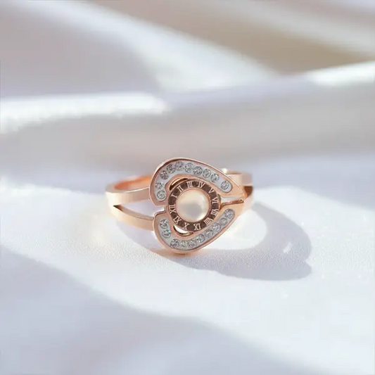 Rose gold pearl halo ring with Roman numeral detailing and sparkling crystals displayed on soft white fabric.